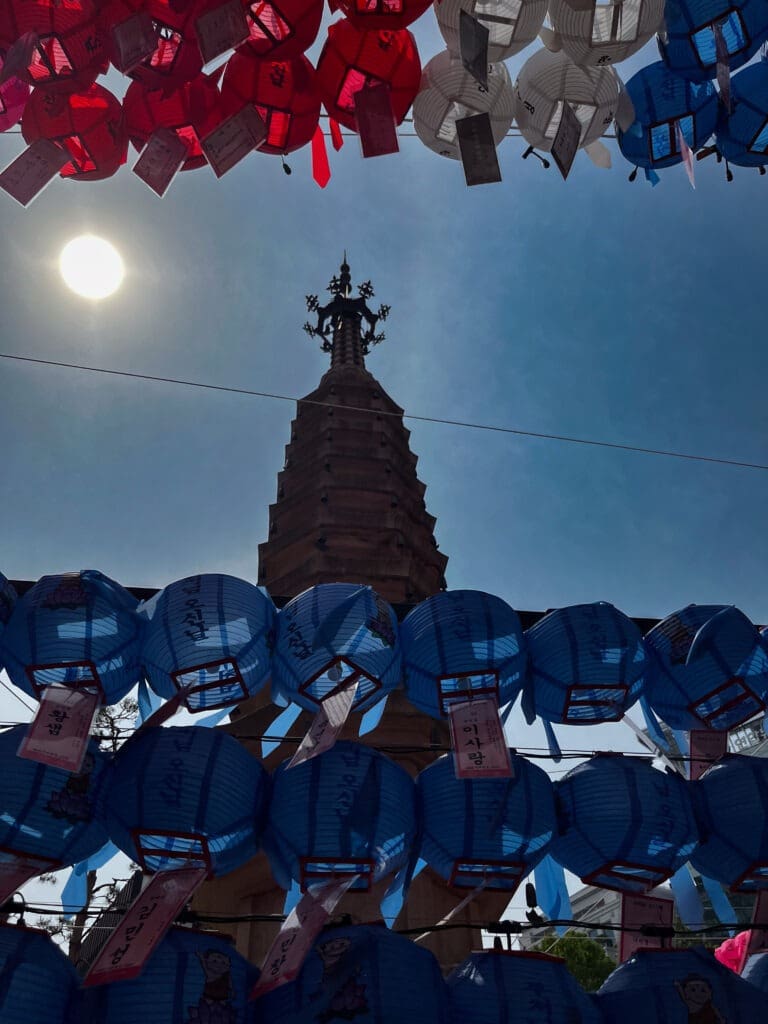 Colorful lanterns frame a historic pagoda tower against a bright sunlit sky, highlighting a cultural celebration or festival scene.